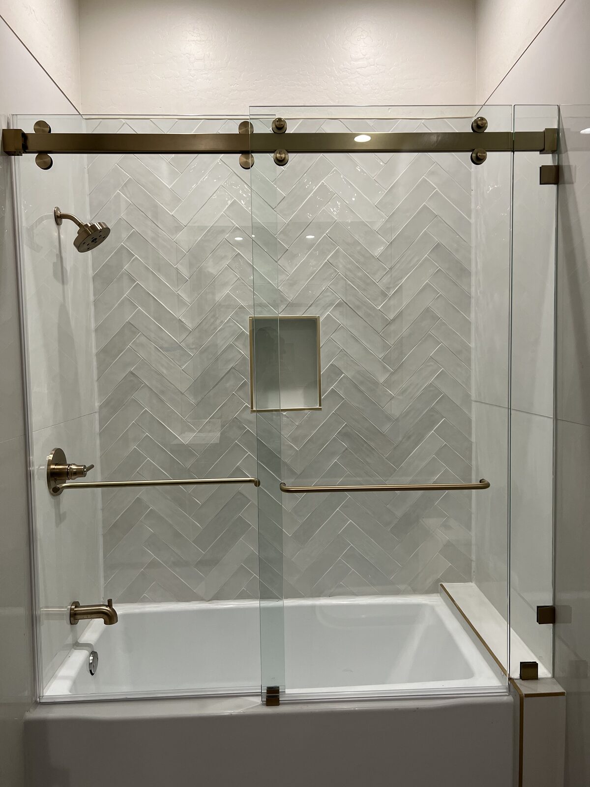 Brass barn style sliding shower door over a herringbone tile tub