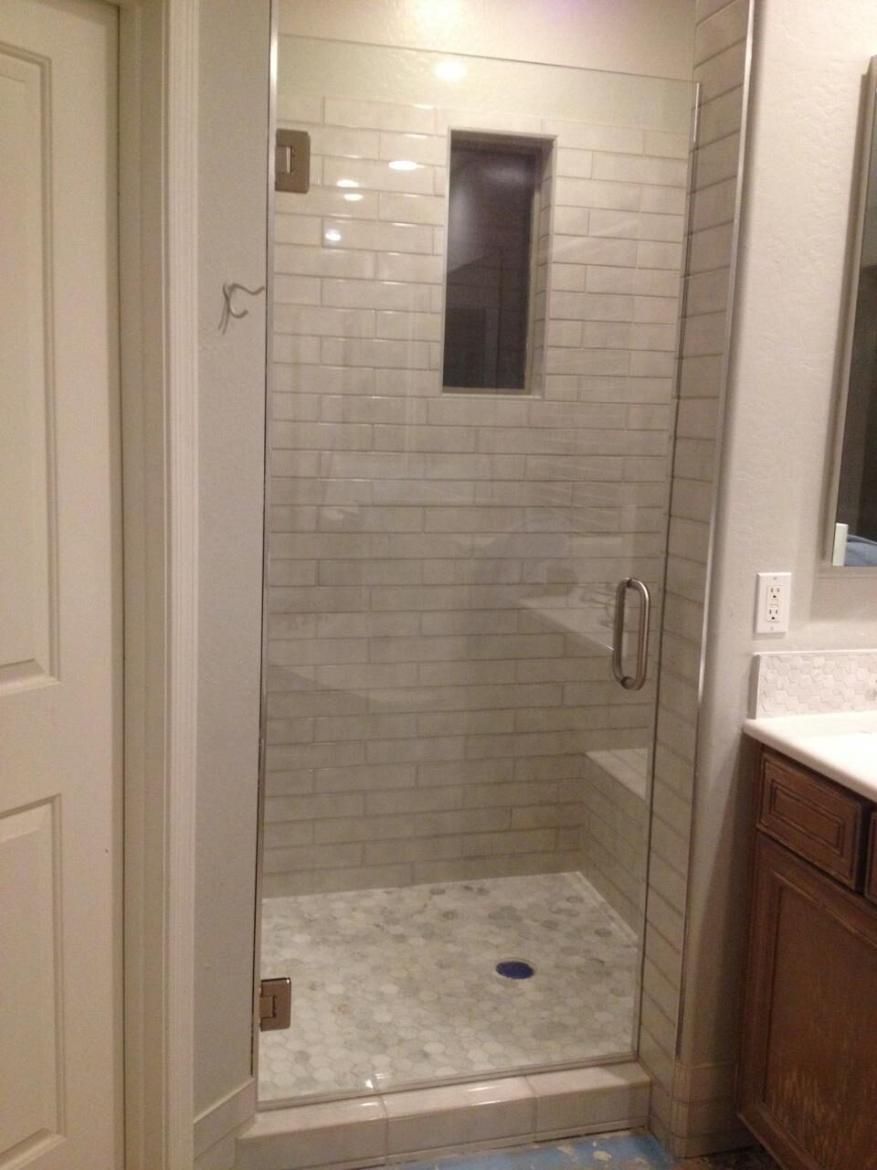 Single hinged glass shower door on a tiled corner shower with seat