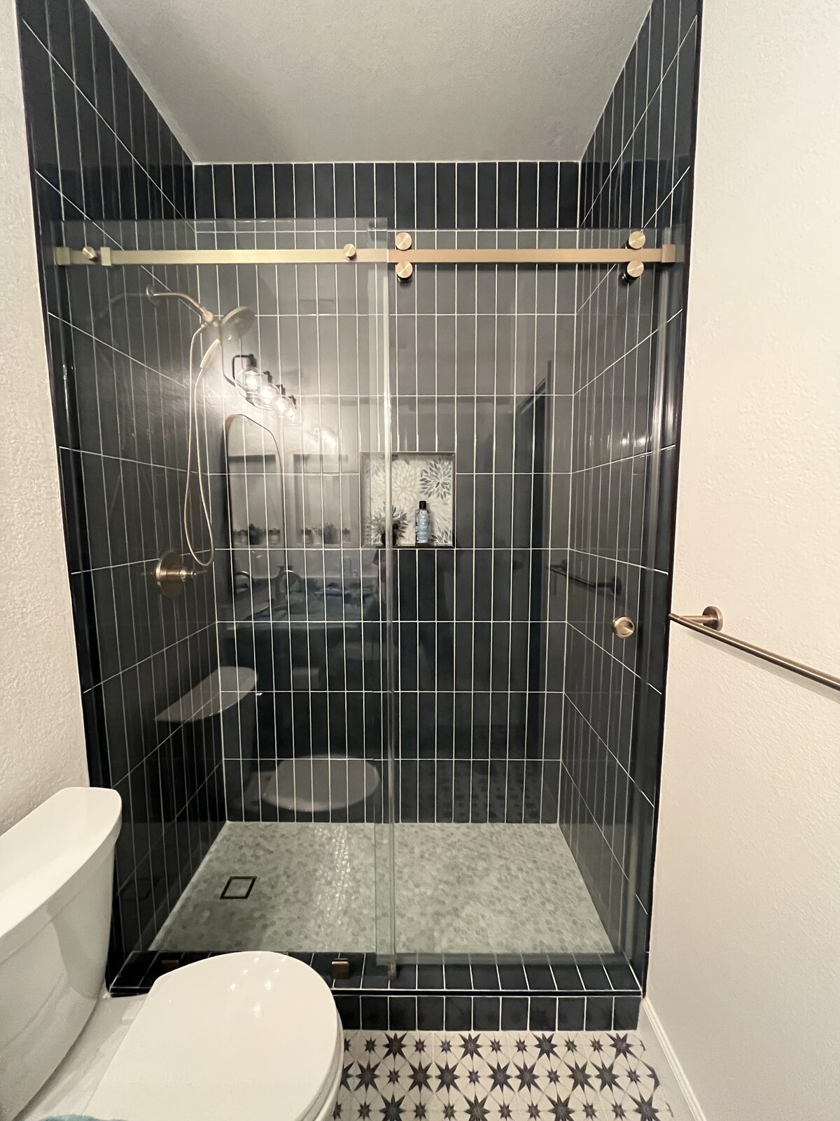 Barn style sliding shower door with gold hardware over a dark vertical tile shower