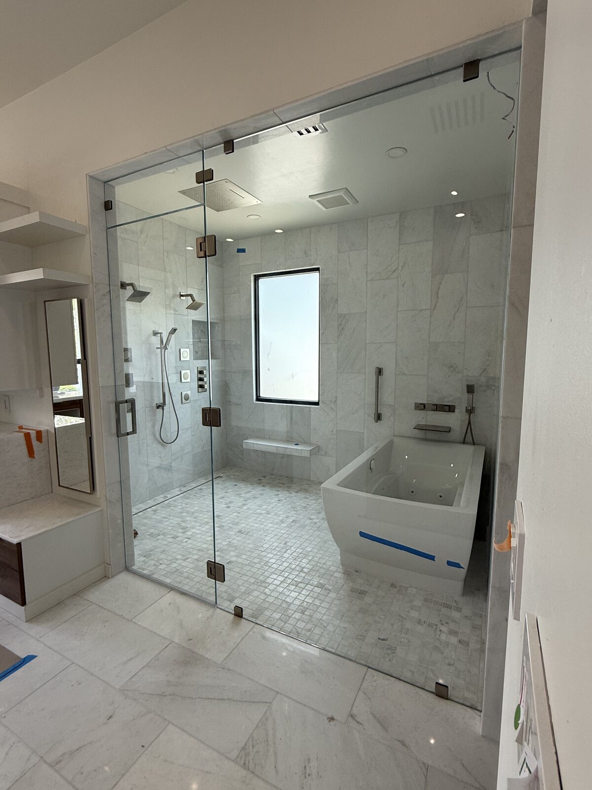 Large marble steam room with soaking tub enclosed behind frameless glass