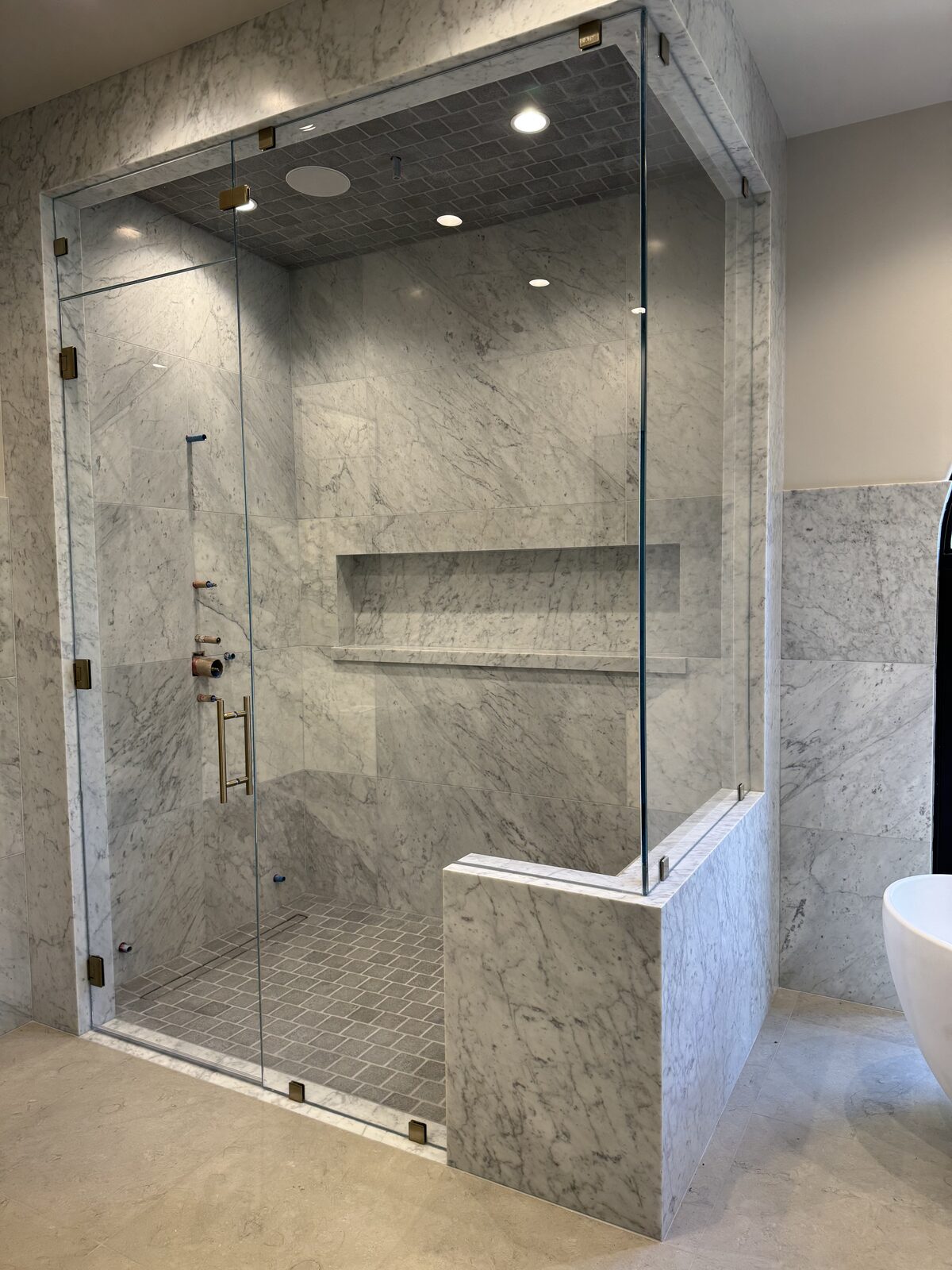 Frameless marble steam shower with built-in bench, lit niche, and full-height sealed glass