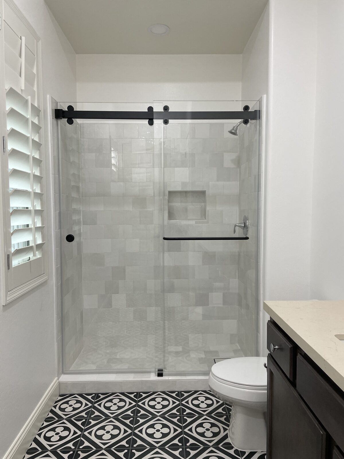 Dark tile walk-in shower with sliding glass panel and gray plank floor