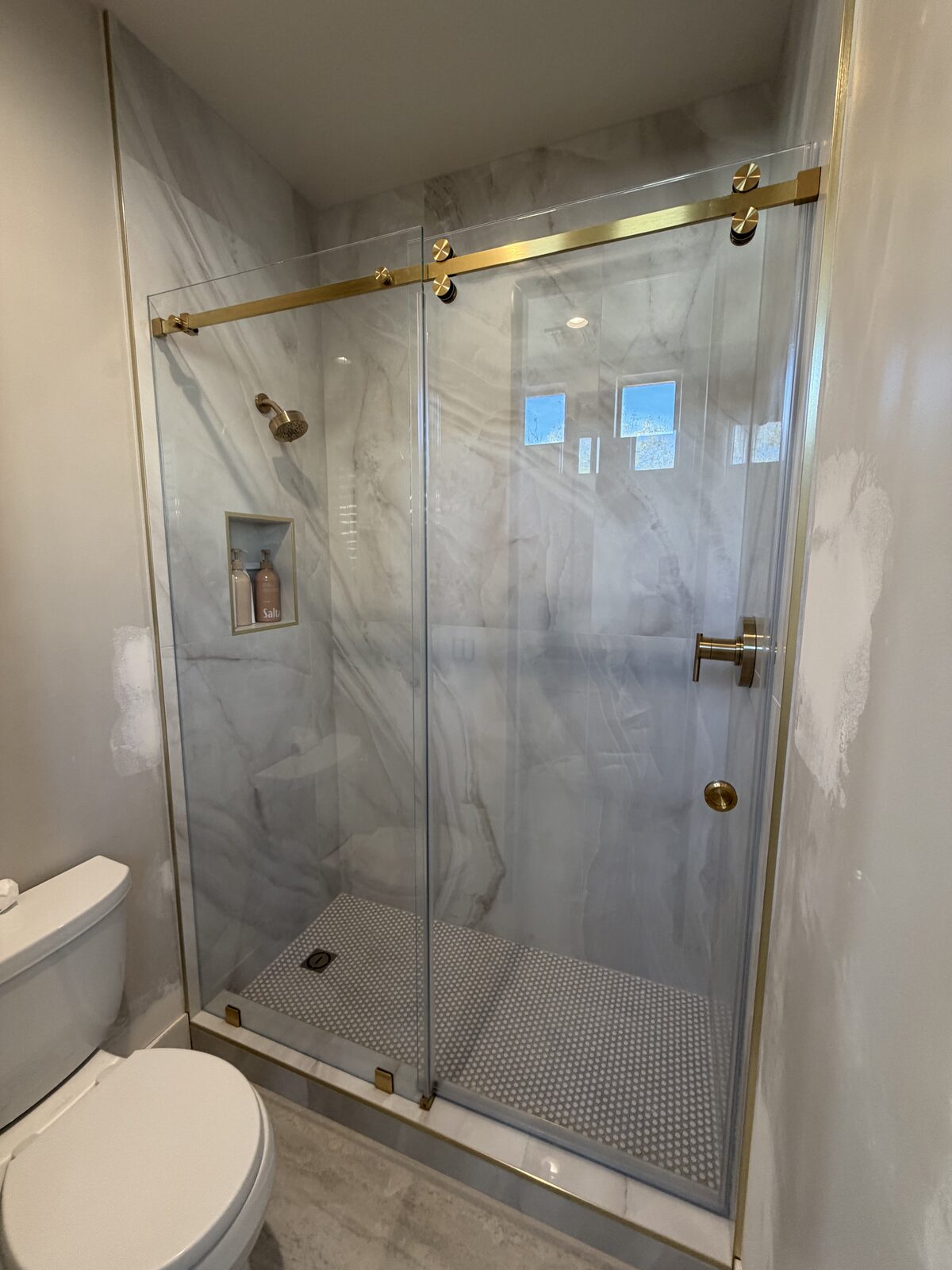 Brushed nickel barn style slider on a corner shower with hexagon floor tile