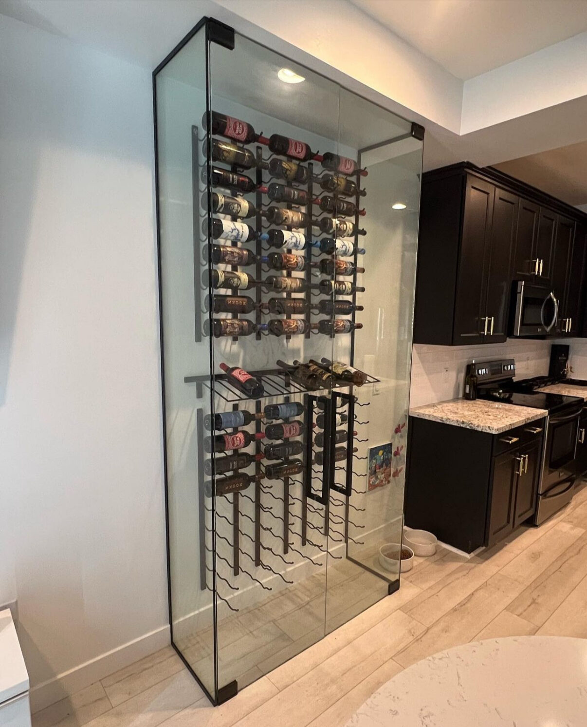 Glass enclosed wine display beside a kitchen with black hardware
