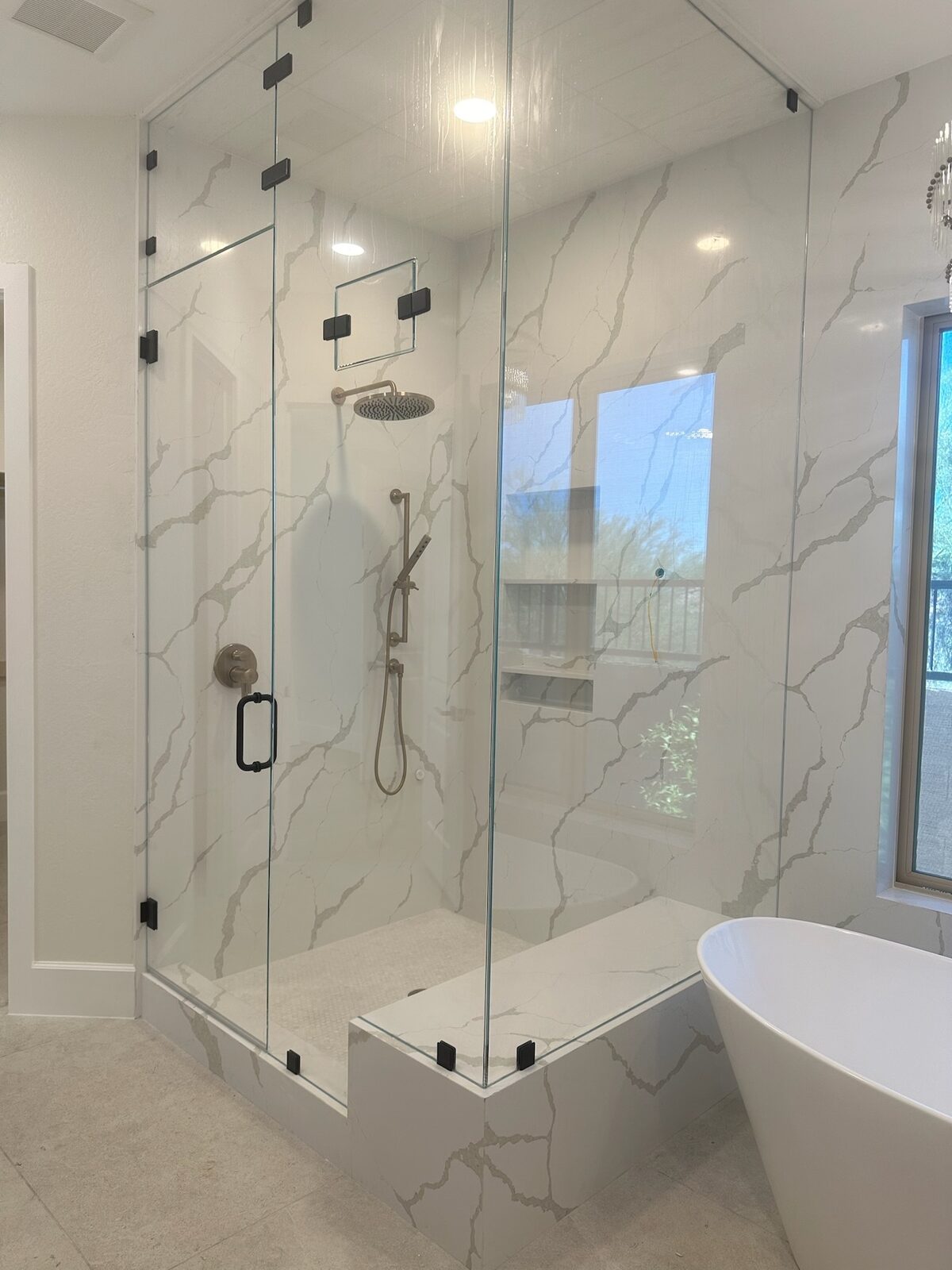 White marble steam shower enclosure with tiled bench and rain head