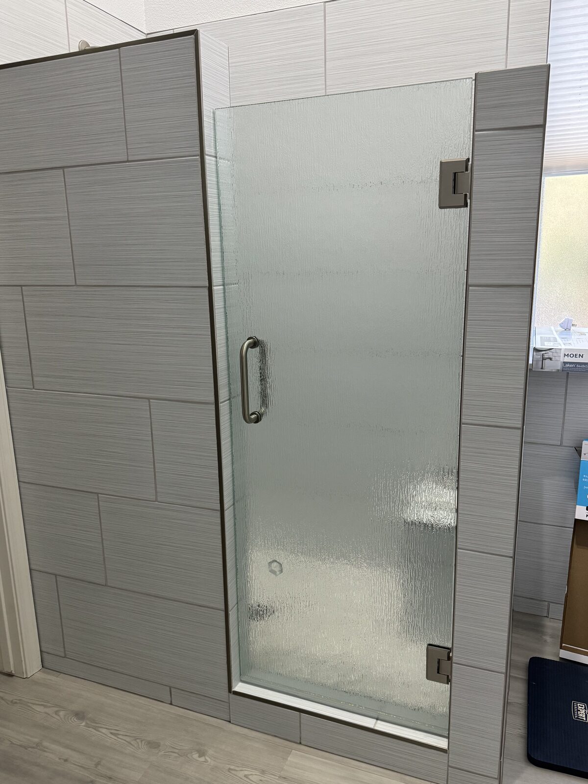 Rain glass single hinged shower door with brushed nickel handle and gray tile