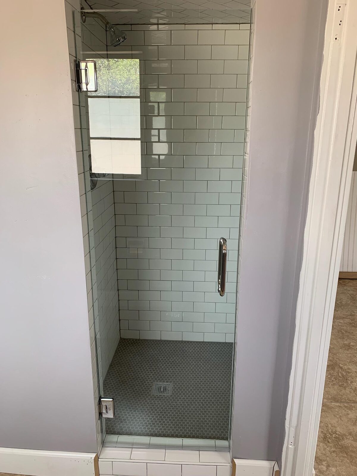 Narrow subway tile shower with single frameless hinged glass door