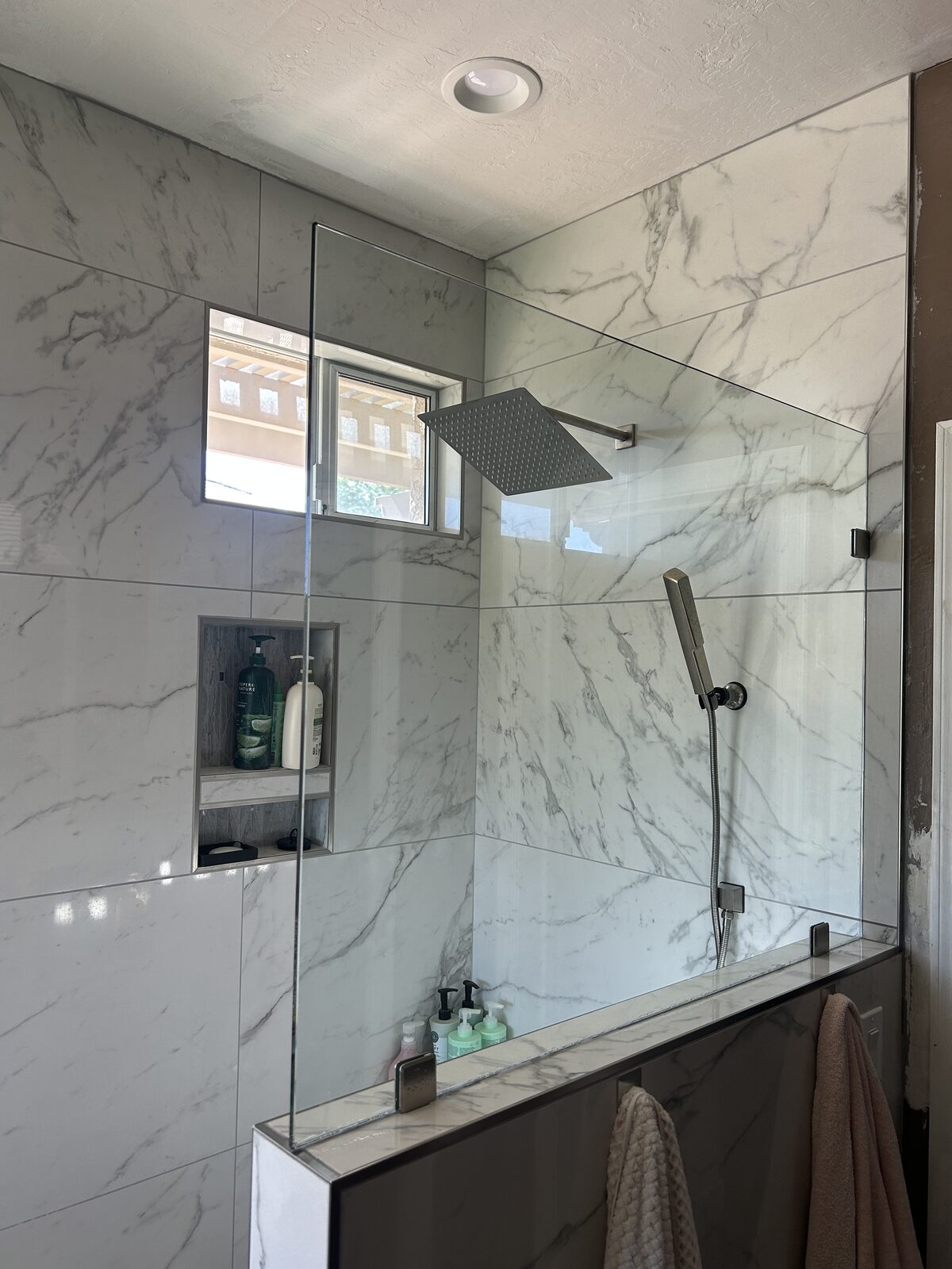 Marble shower with fixed glass panel above a tiled half wall