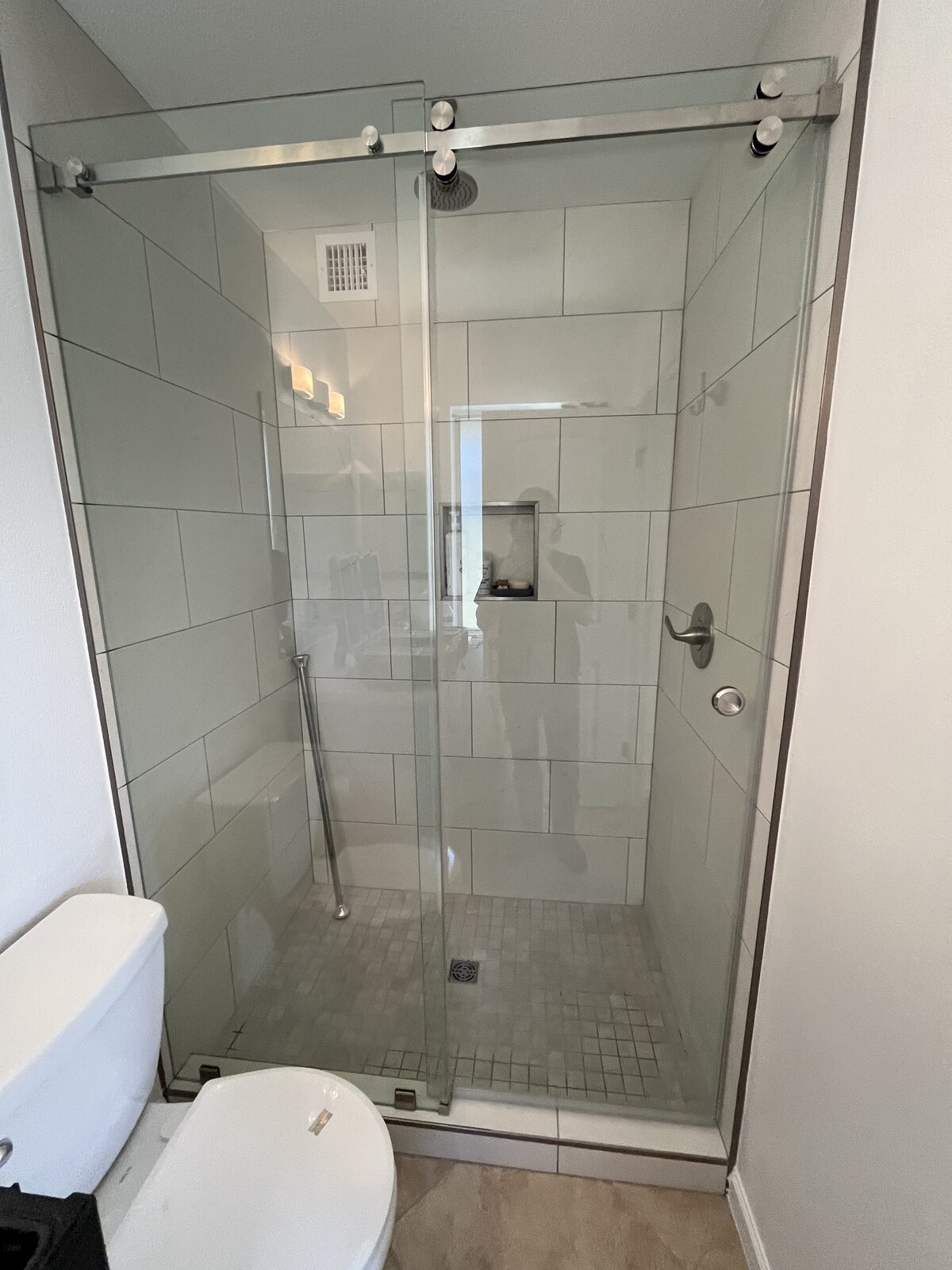 Barn style sliding shower door with nickel rail on a corner shower